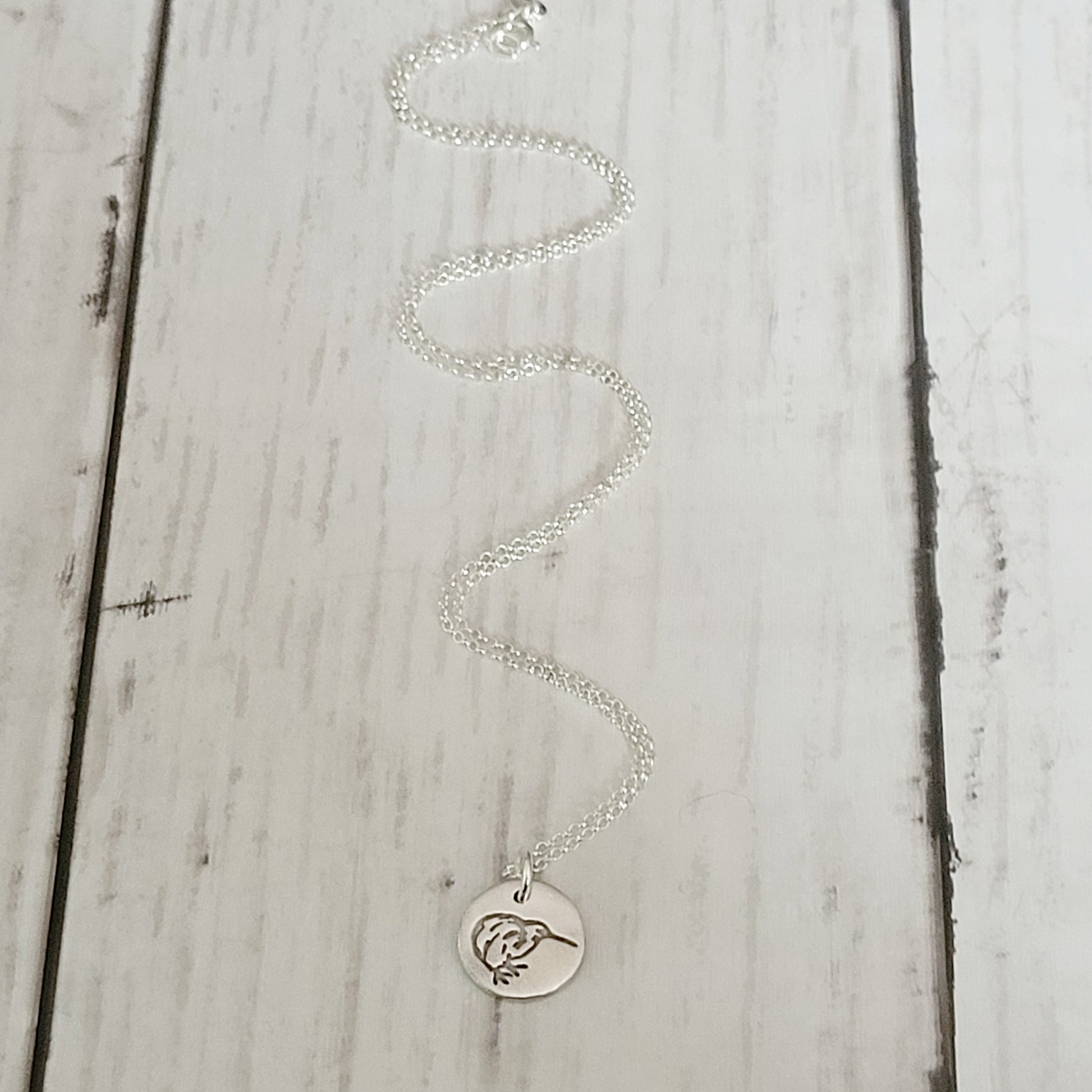 Silver kiwi bird necklace with a round pendant on a light wooden surface