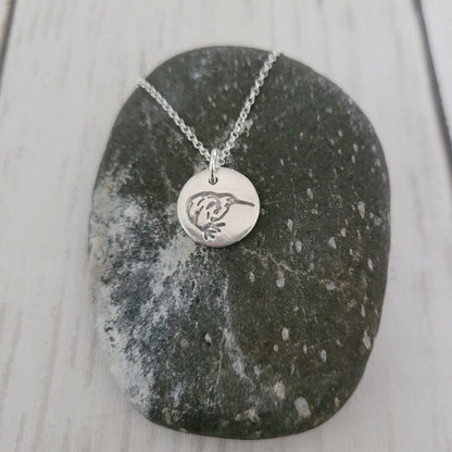 Silver necklace with a round pendant on a dark stone surface