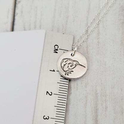 Silver necklace with a kiwi bird pendant on a ruler for scale