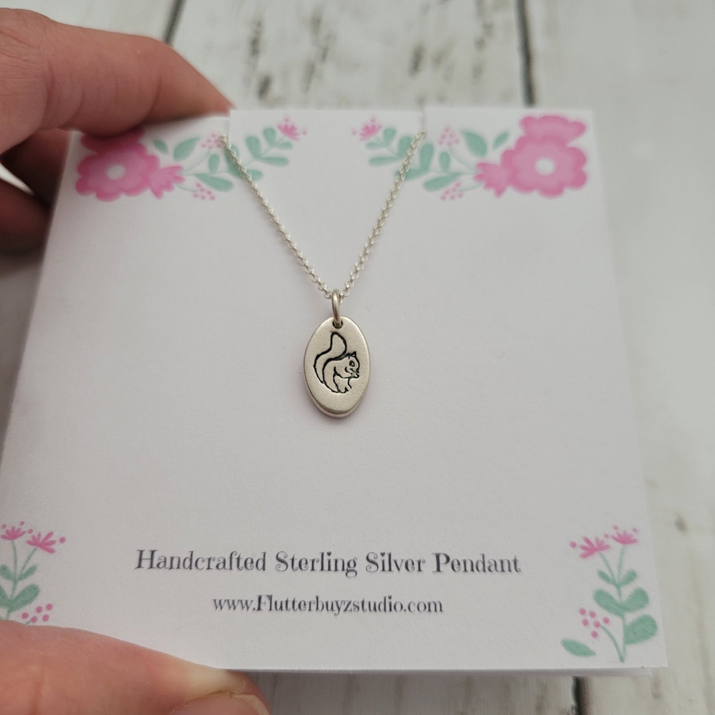 Handcrafted sterling silver squirrel pendant on a floral card