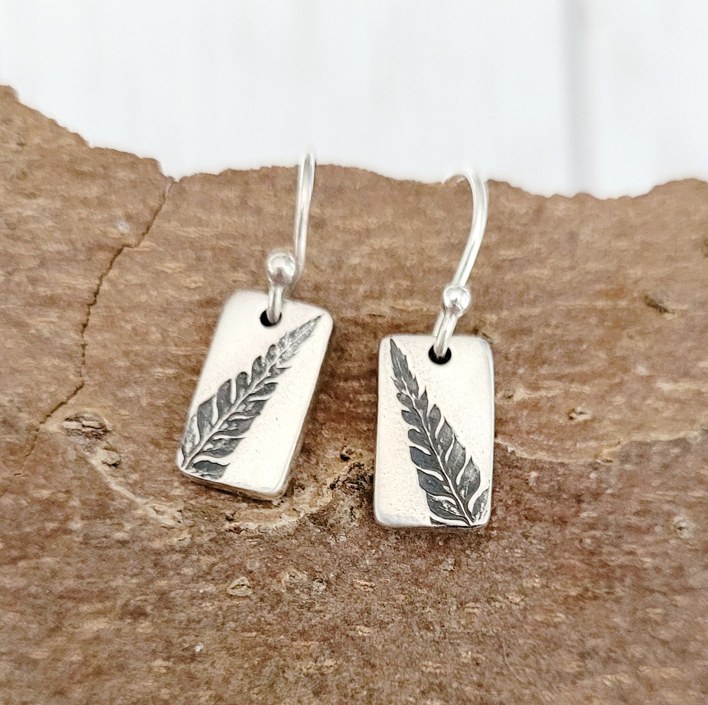 silver fern earrings forward on wooden bark surface