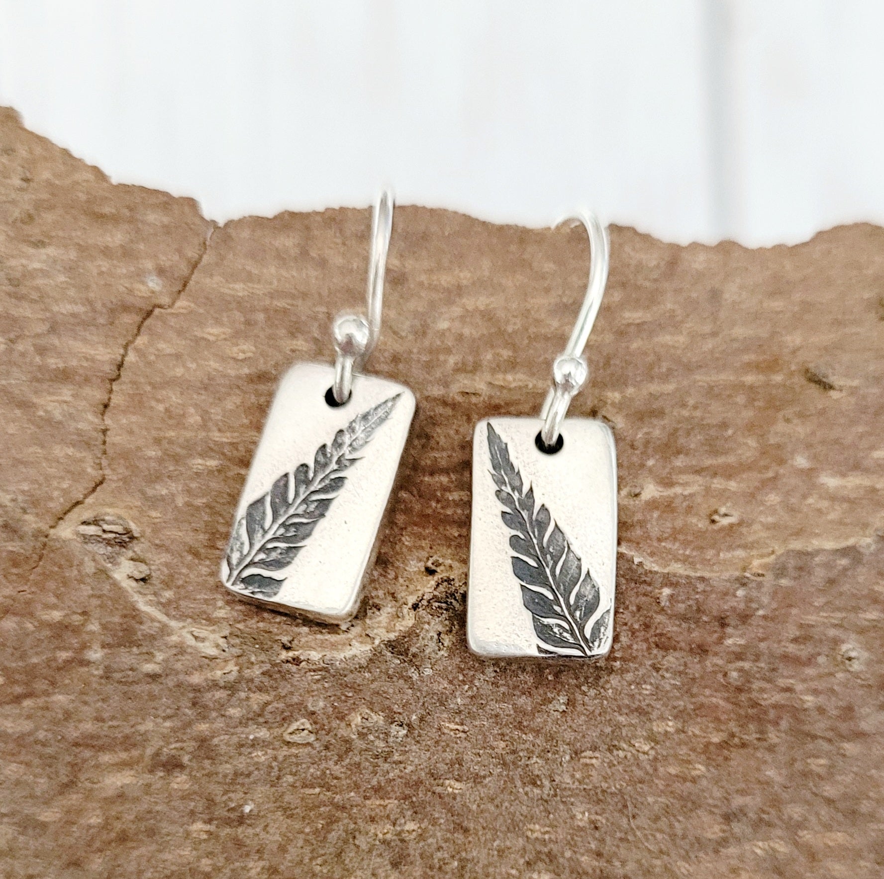 silver fern earrings forward on wooden bark surface