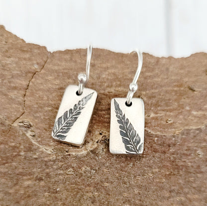 silver fern earrings forward on wooden bark surface