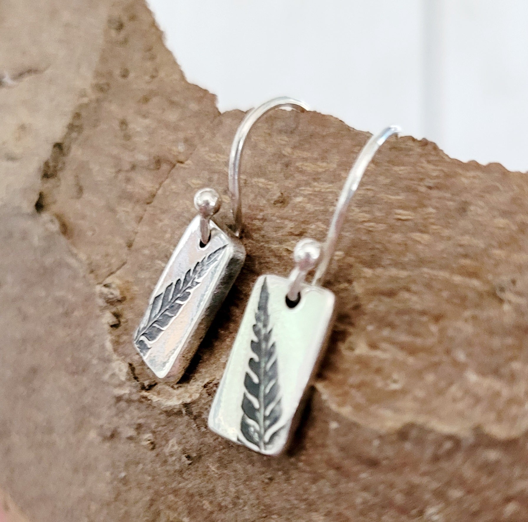 silver leaf design earrings side view on wooden surface