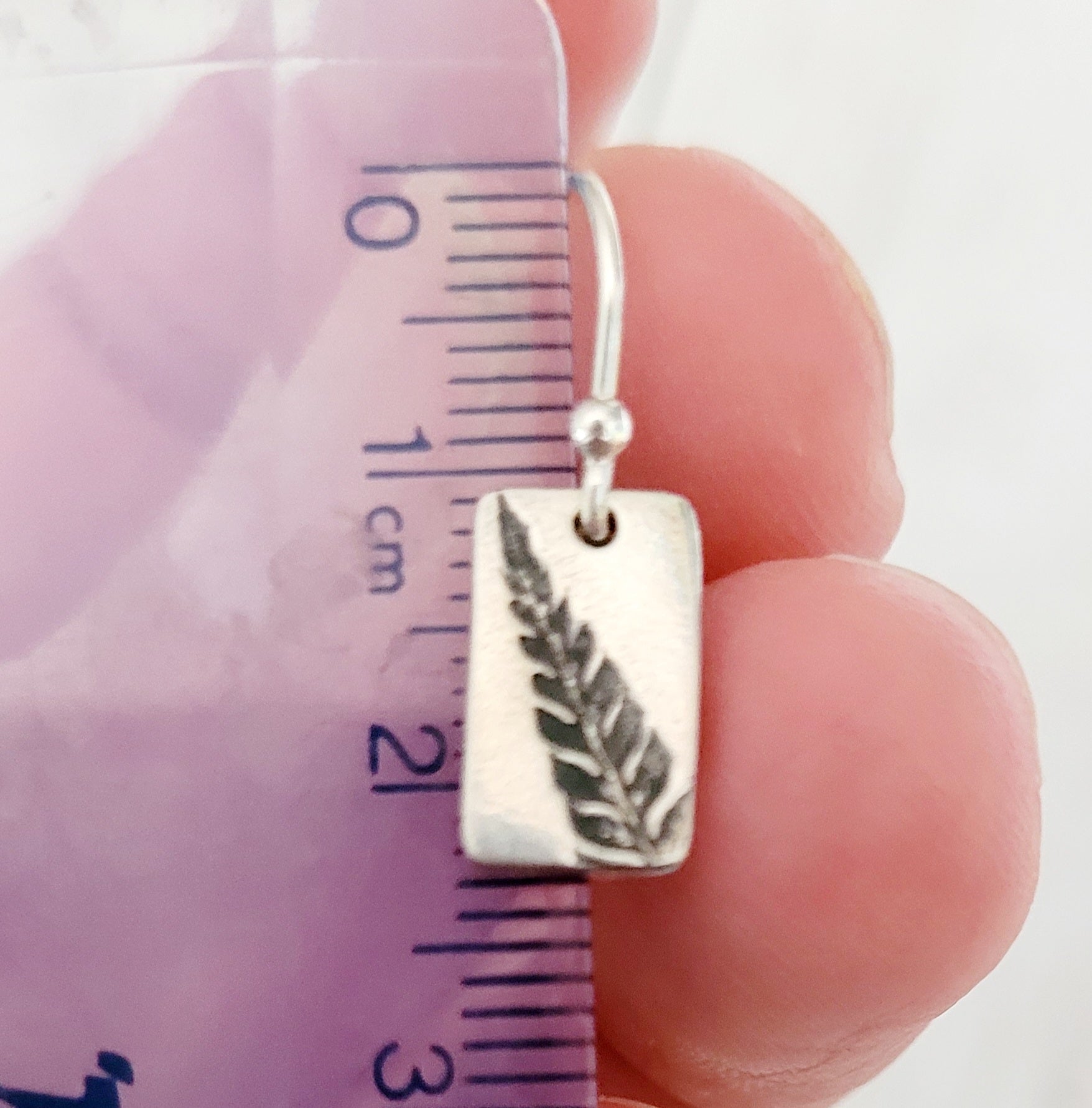 Silver earring with leaf design held against a measuring ruler.