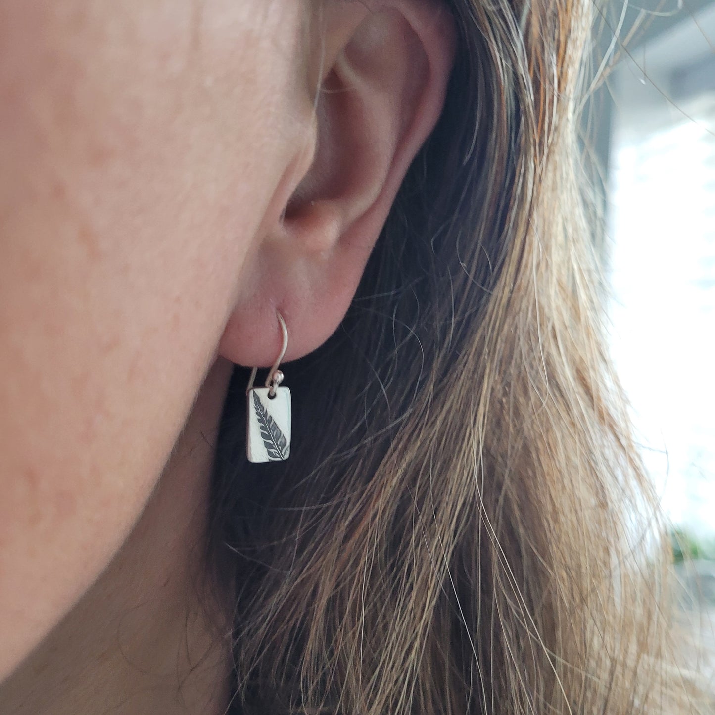 close up of an ear wearing fern leaf silver reactangular earrings