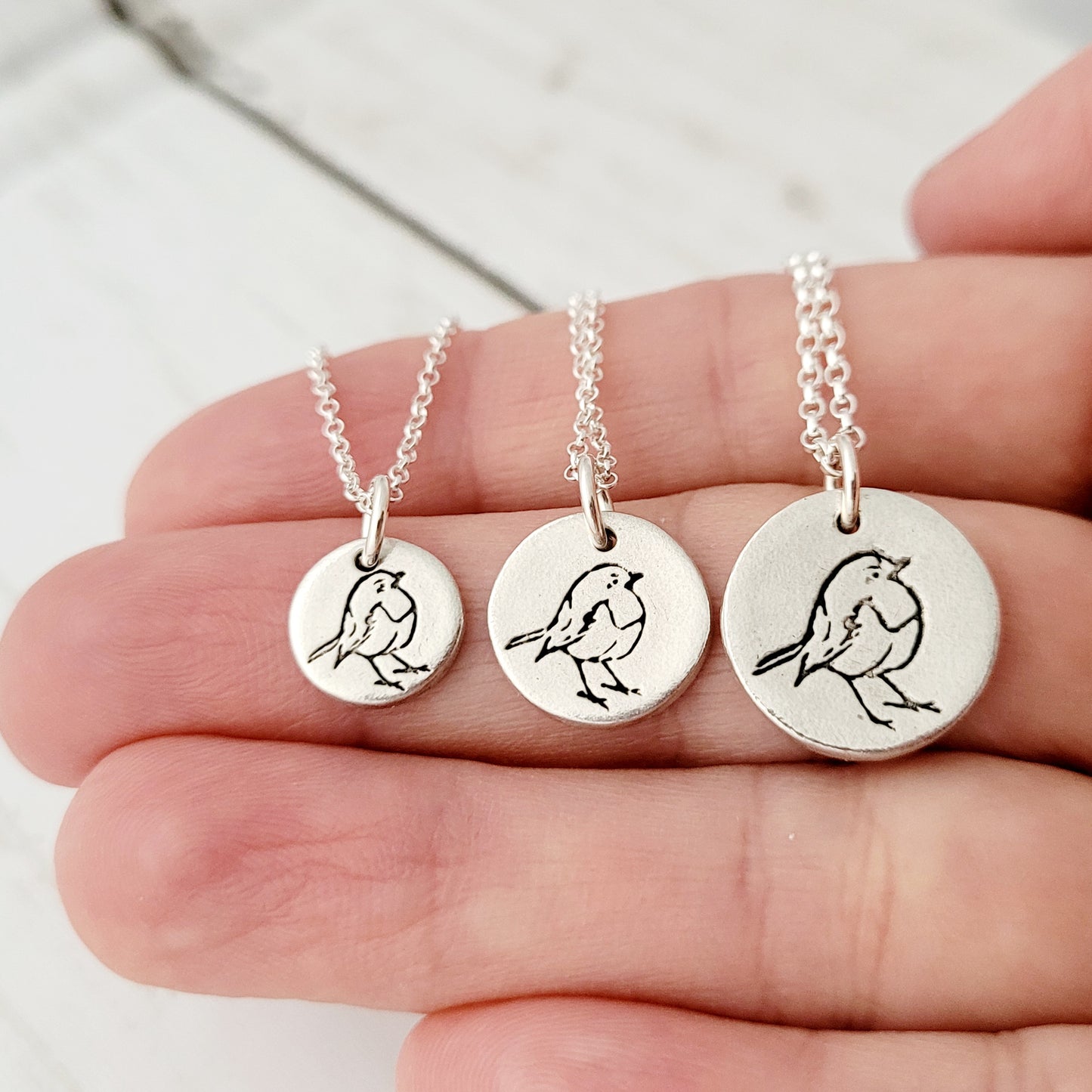 Three silver necklaces with bird pendants on a hand against a light background