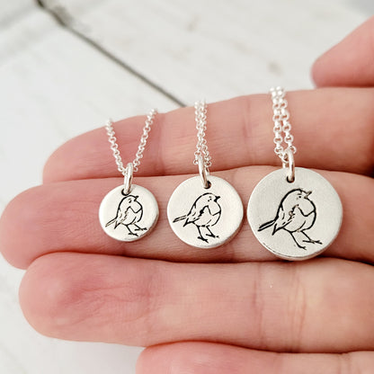Three silver necklaces with bird pendants on a hand against a light background