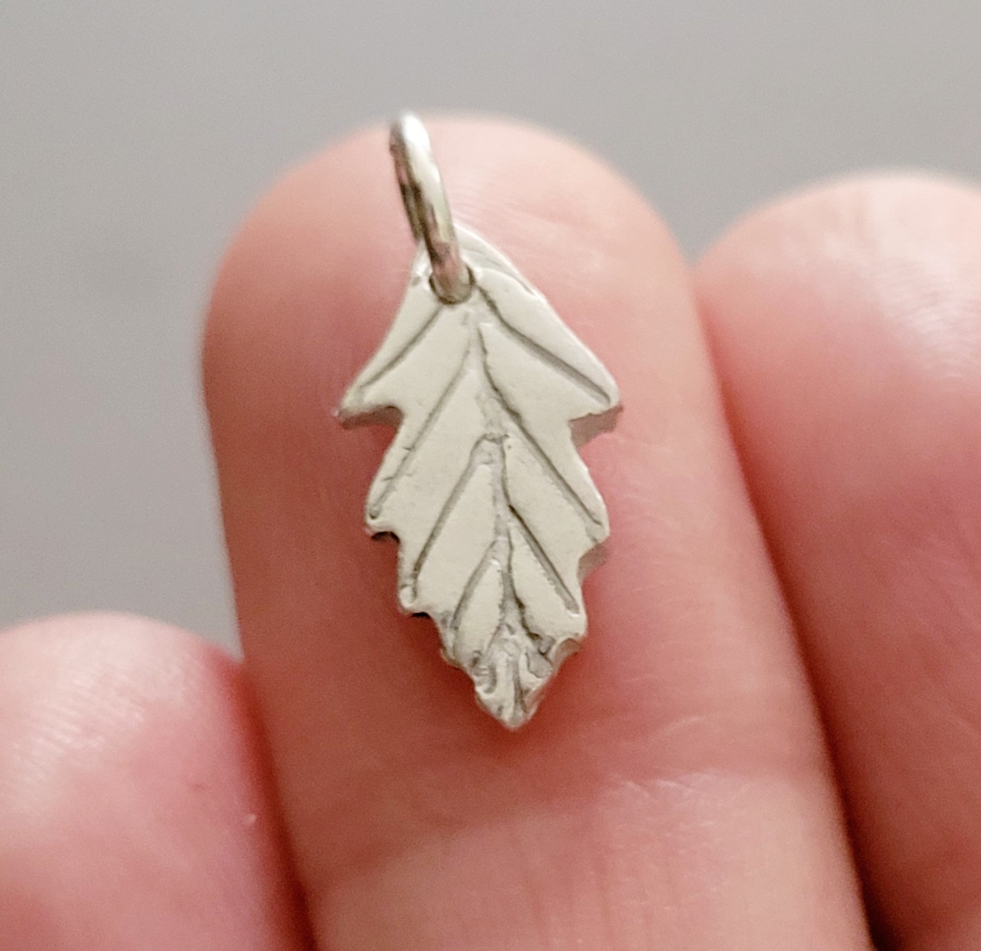 tiny silver leaf charm being held on finger