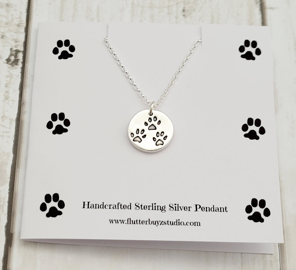 three paw prints on round silver pendant shown on a paw print card - flutterbuyzstudio