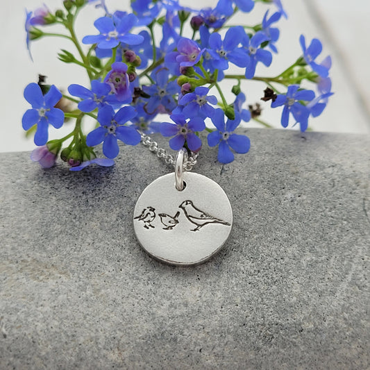 3 birds on round pendant against stone
