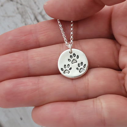 three paw prints on round silver pendant