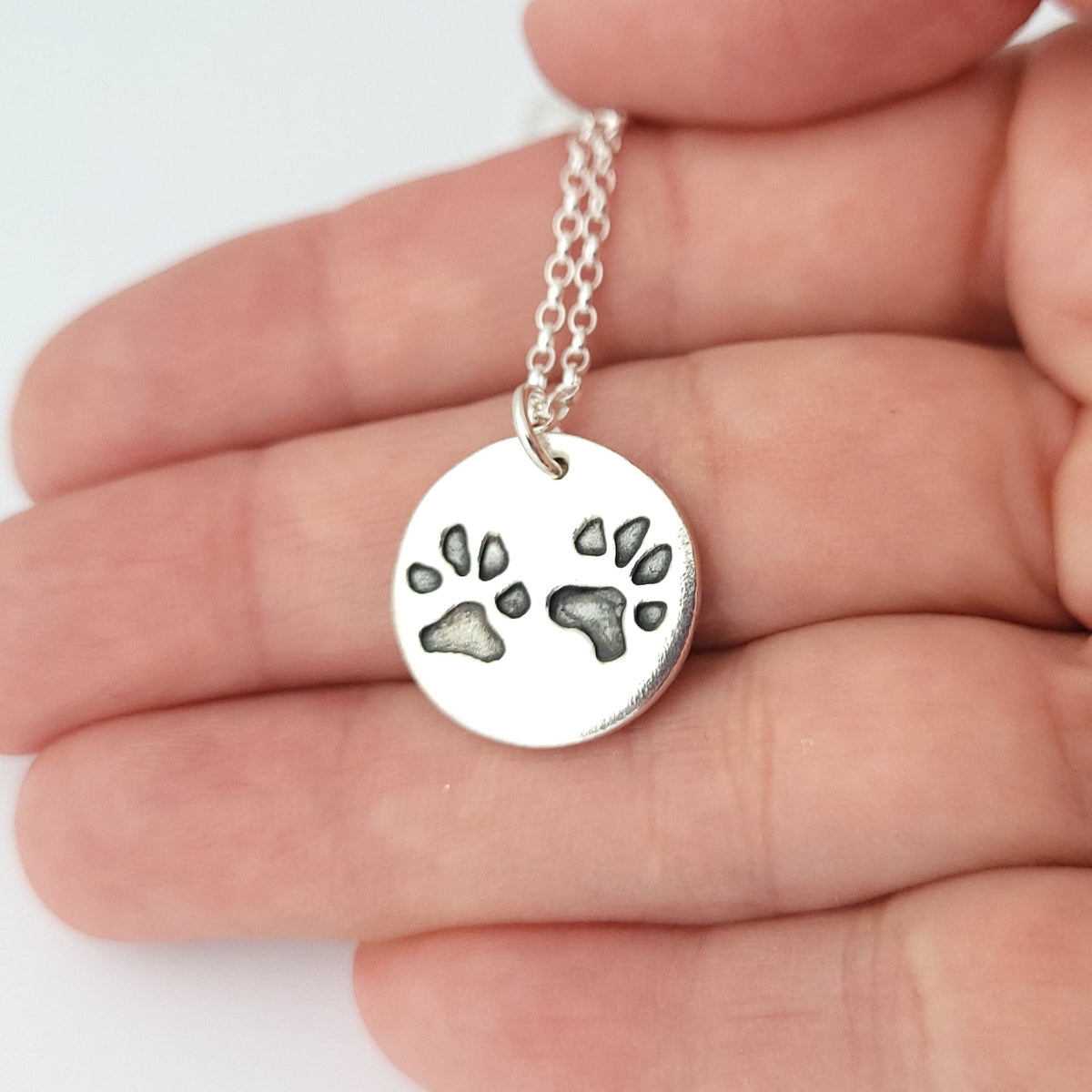 two paw prints on a round pendant being held