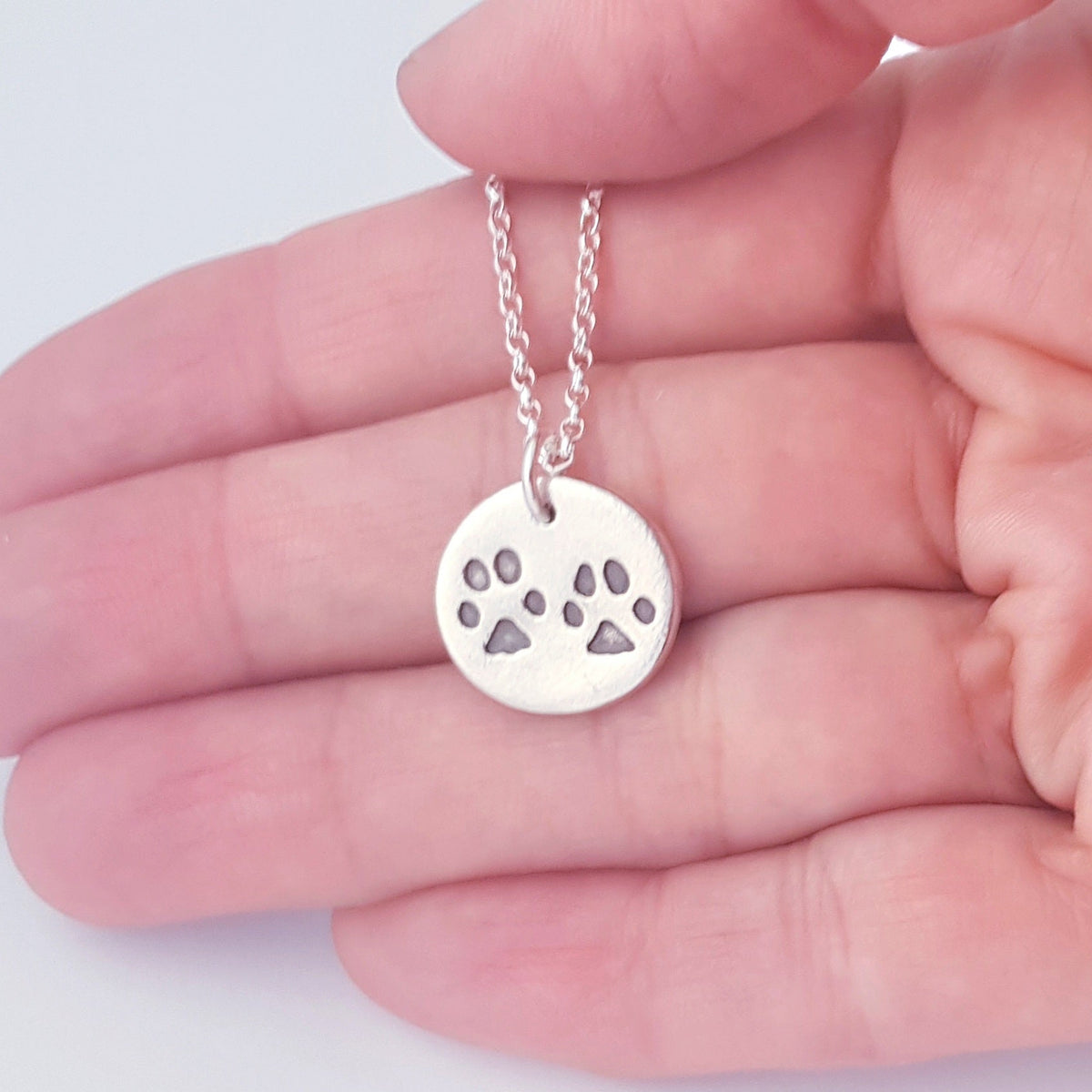 round silver paw print pendant being held