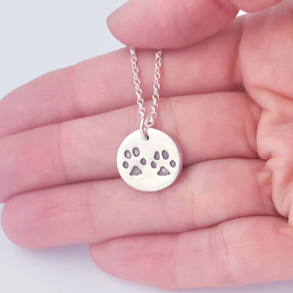 round silver paw print pendant being held