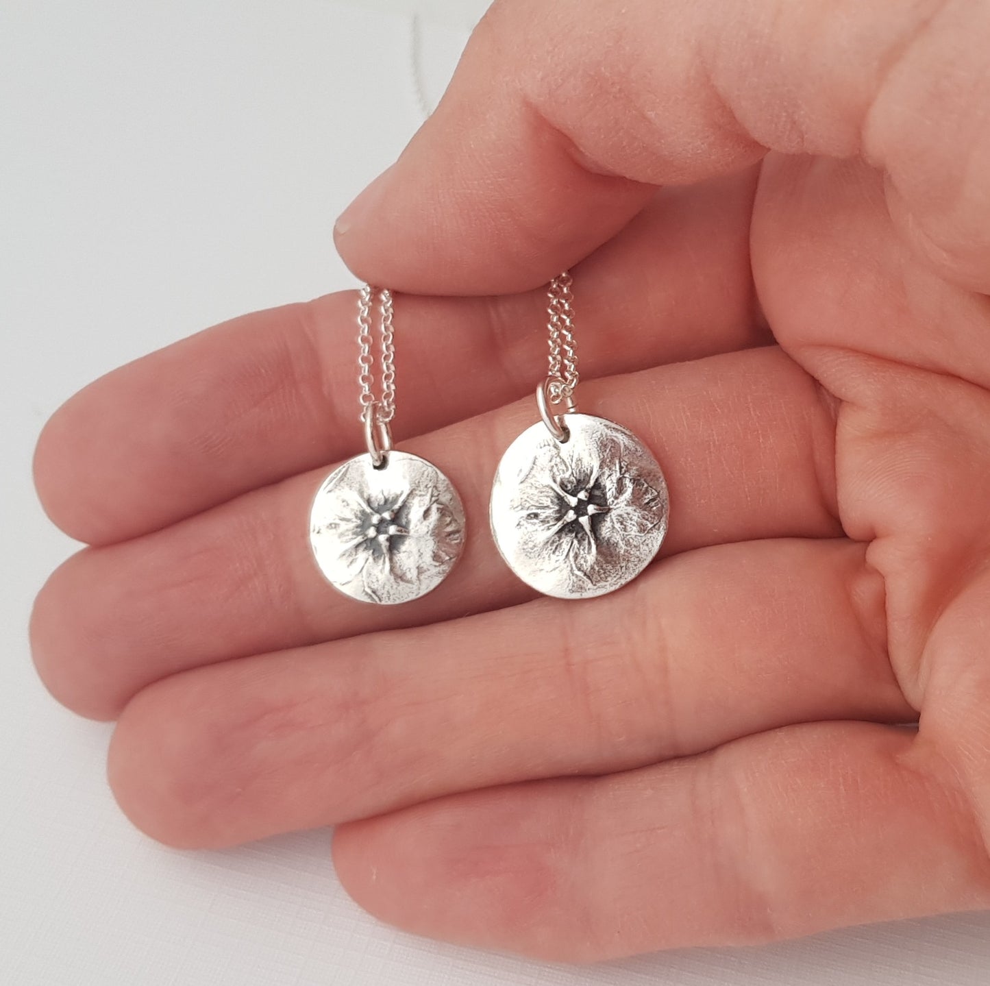 Silver floral green alkanet pendants held in a hand against a white background
